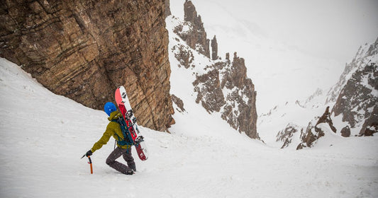 Splitboard mountaineer with a Weston Ridgeline Splitboard on his back and holding an ice axe while climbing a snowy steep mountain couloir