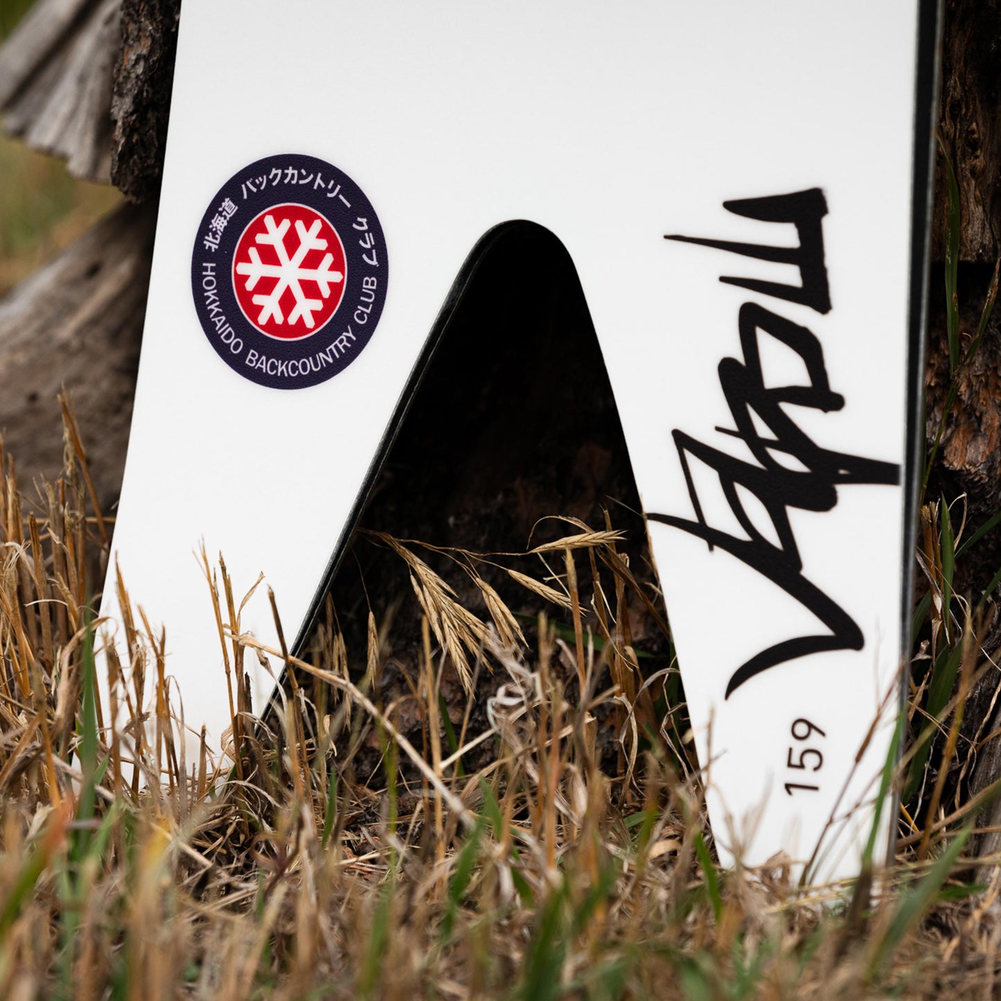 Close up image of the weston japow snowboard x hokkaido backcountry club limited edition swallowtail featuring a white graphic on the ground surrounded by grass