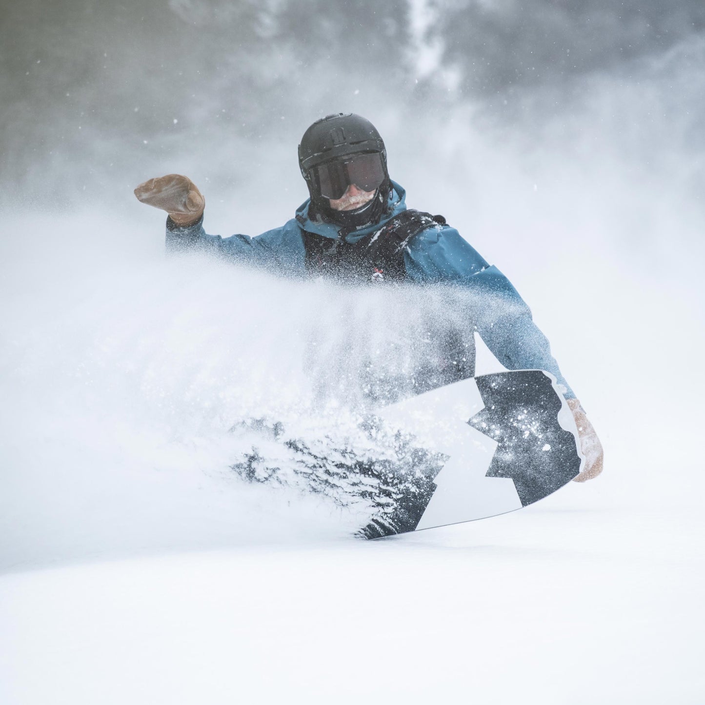 snowboarder riding the weston hatchet making a heelside turn in deep powder spraying snow into his face