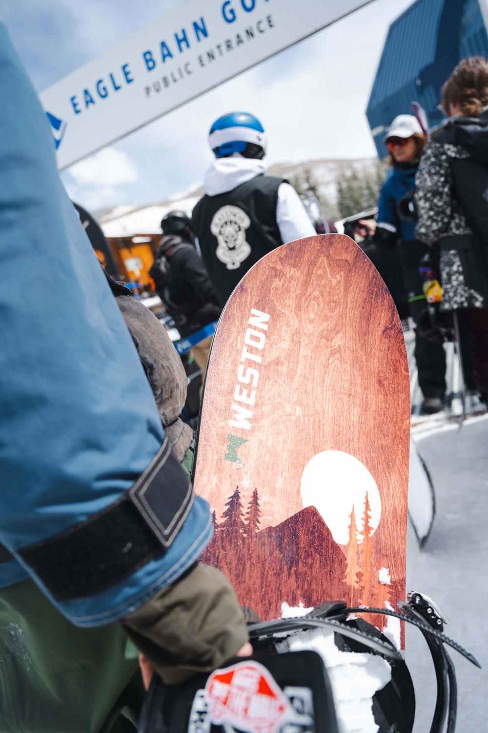 Snowboarder standing in the lift line at a ski resort holding the Weston backwoods snowboard