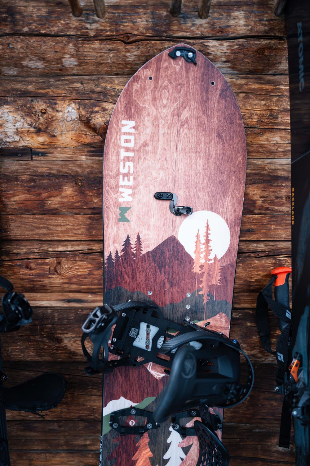 The weston backwoods splitboard with a wooden angular mountain graphic leaning up against a backcountry hut