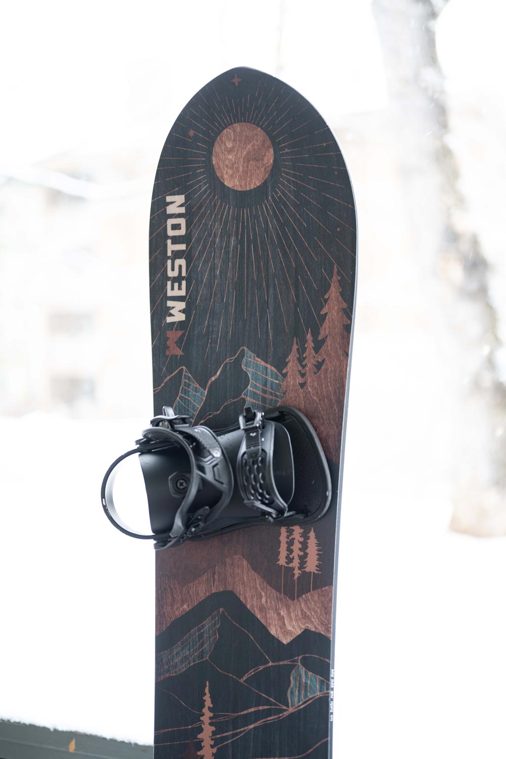 weston eclipse snowboard promiently featuring dark wood grain graphics with an eclipse moon and mountainous forests