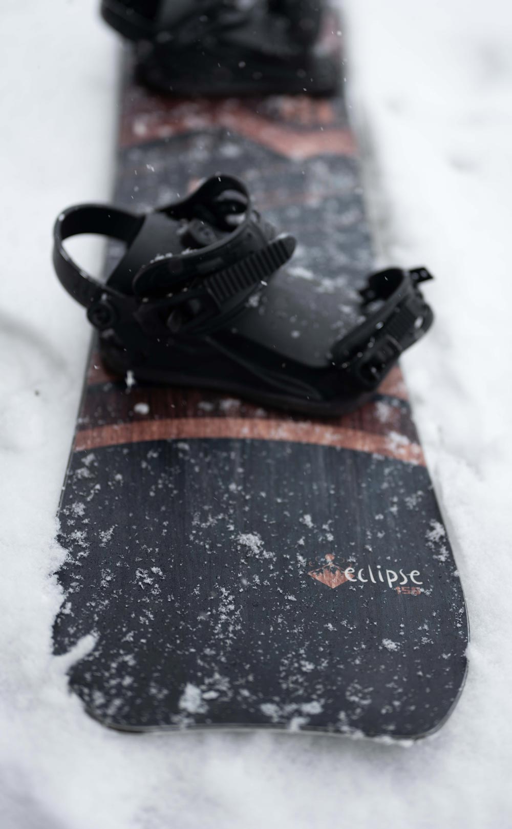 close up image of the crescent moon tail of the weston eclipse snowboard on the snowy ground with a black union snowboard binding