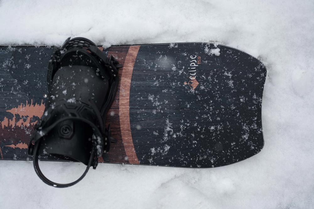 close up image of the crescent moon tail of the weston eclipse snowboard on the snowy ground with a black union snowboard binding