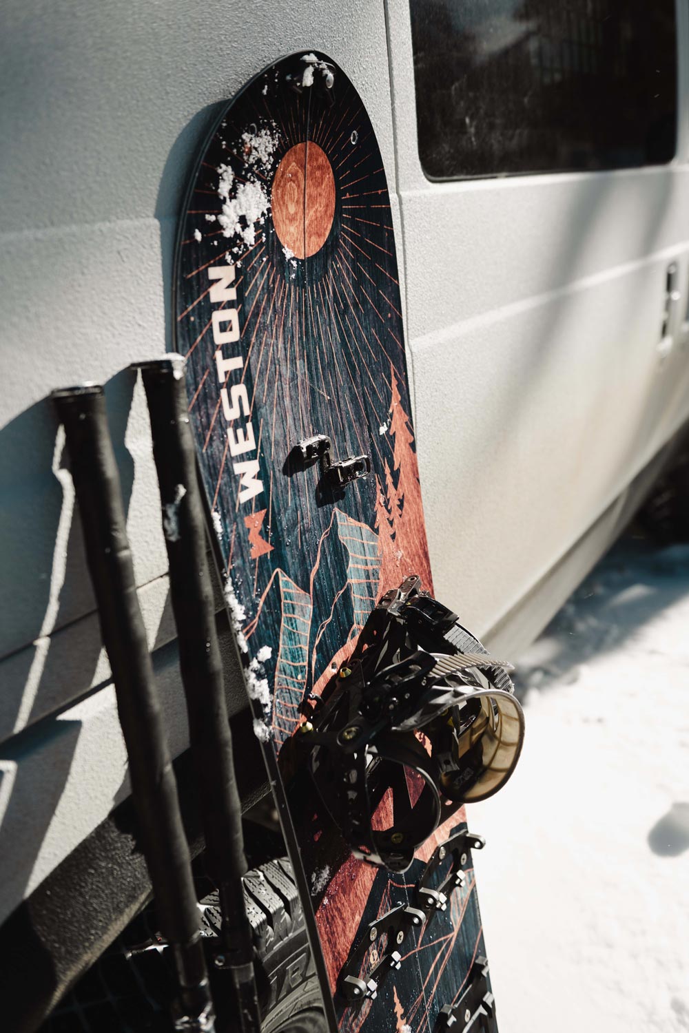 the weston eclipse splitboard featuring a mountainous lanscape and eclipse moon alongside some backcountry touring poles leaned up against a camper van