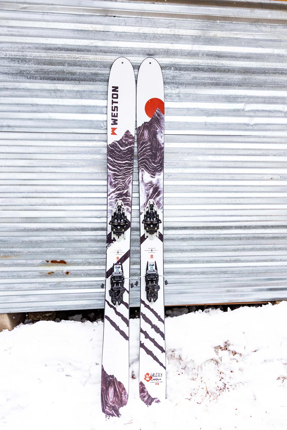a pair of weston grizzly carbon skis learning up against a garage door with snow on the ground