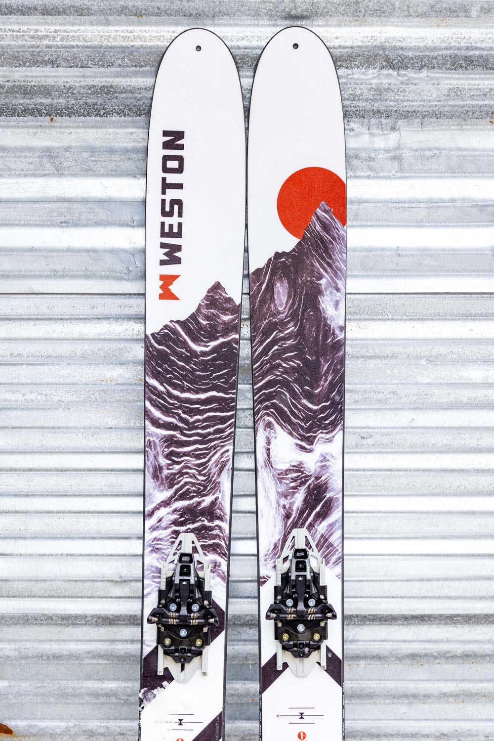 a pair of weston grizzly carbon skis with tech ski bindings leaned up against a garage door