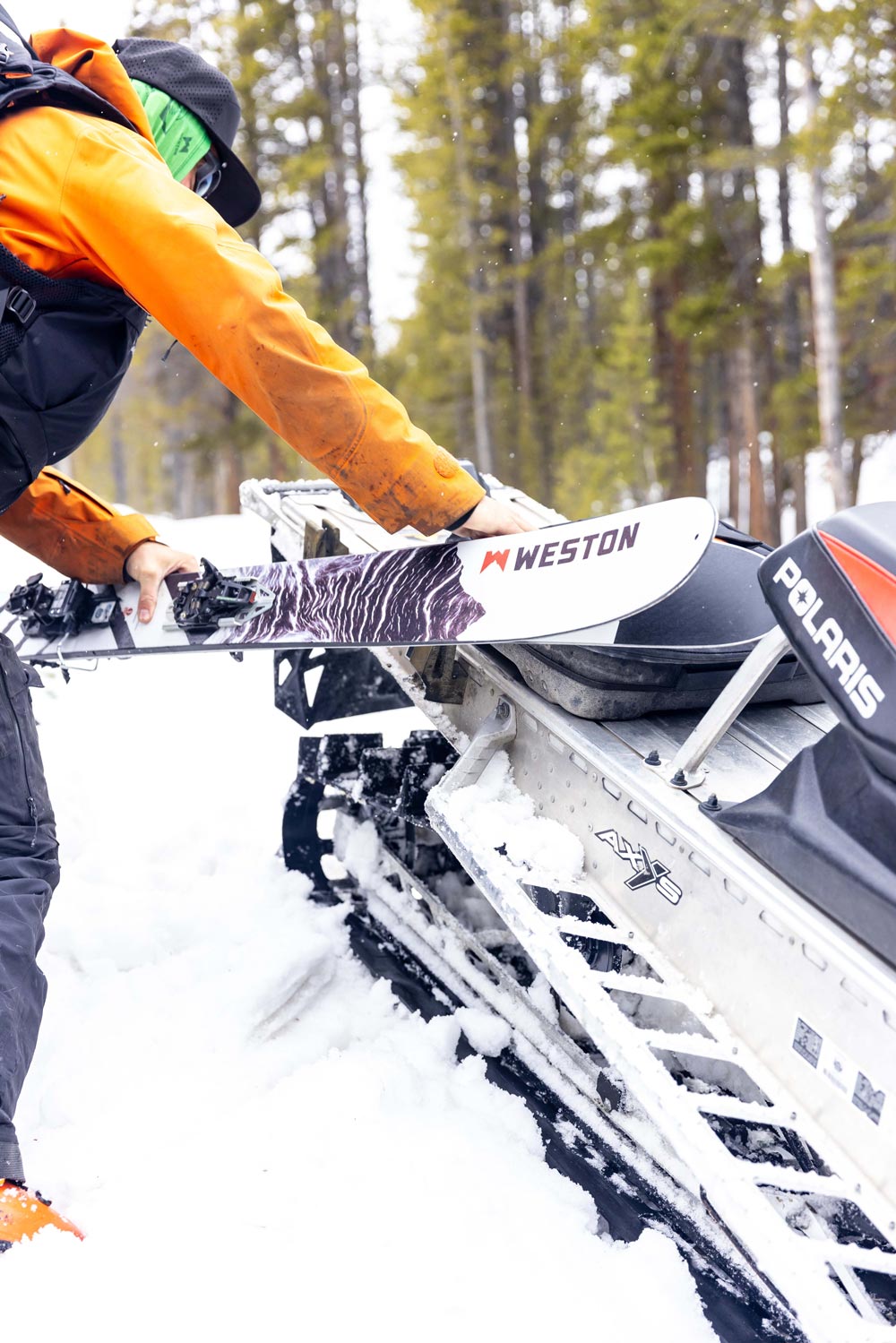 skier strapping a pair of weston grizzly carbon skis to a snowmobile in the snow