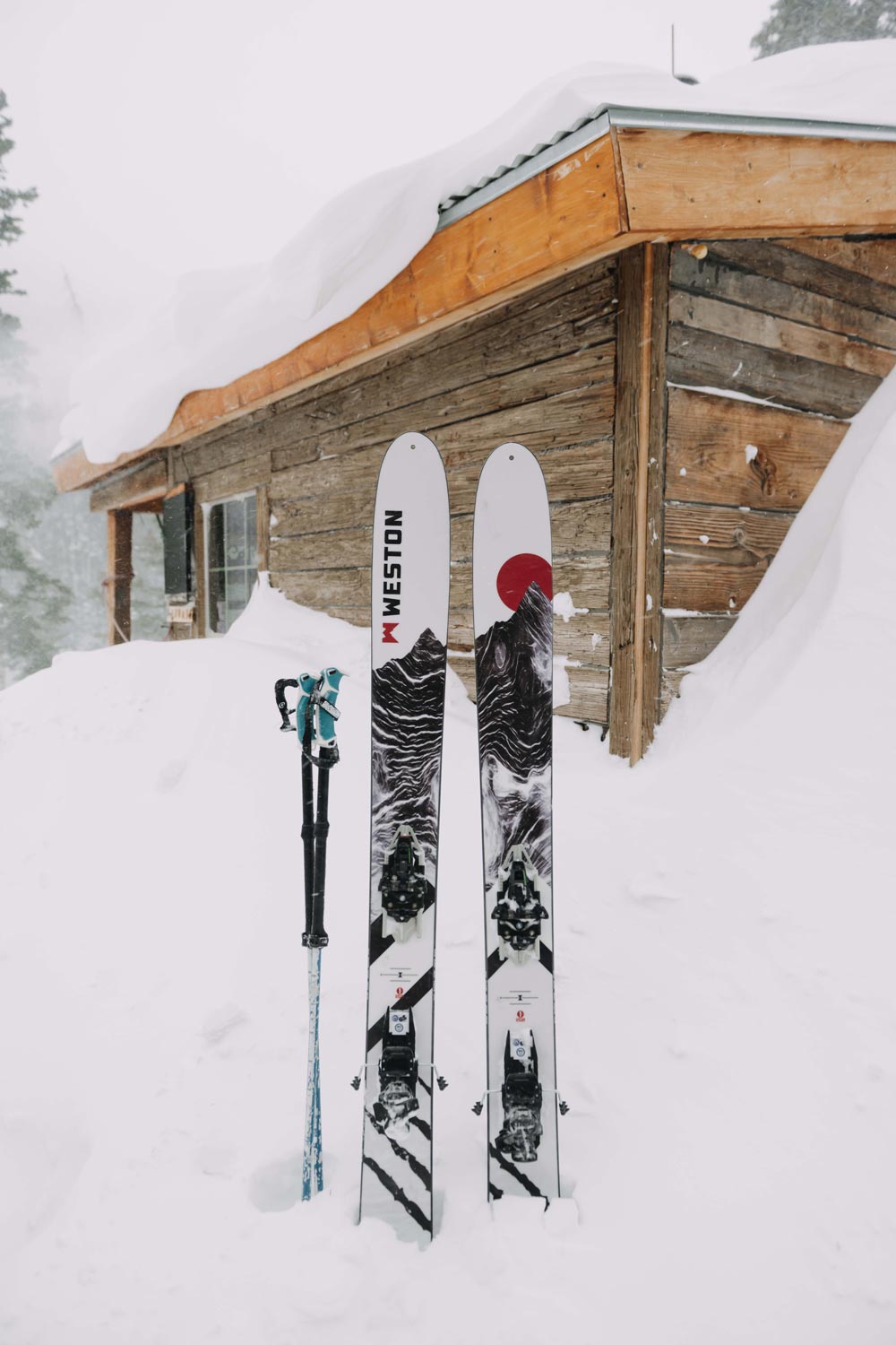 a pair of weston grizzly carbon skis and ski poles stuck in the snow in front of a backcountry hut