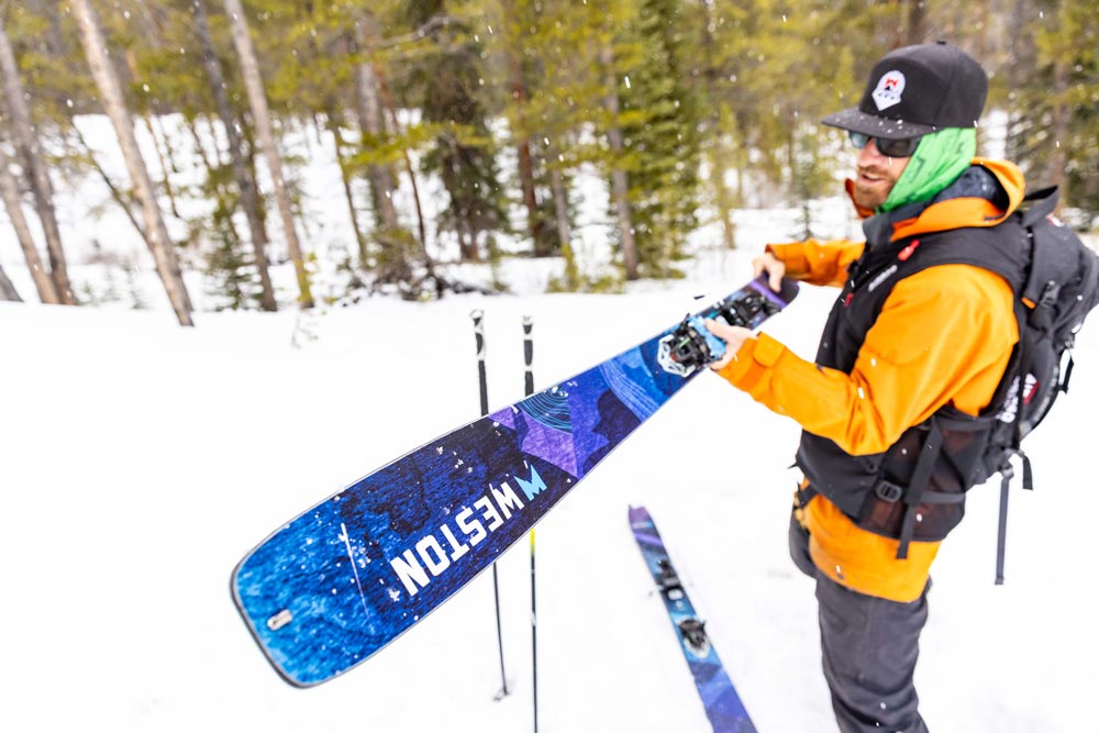 skier with a black hat and sunglasses holding the weston skyline skis out in a snowy forest