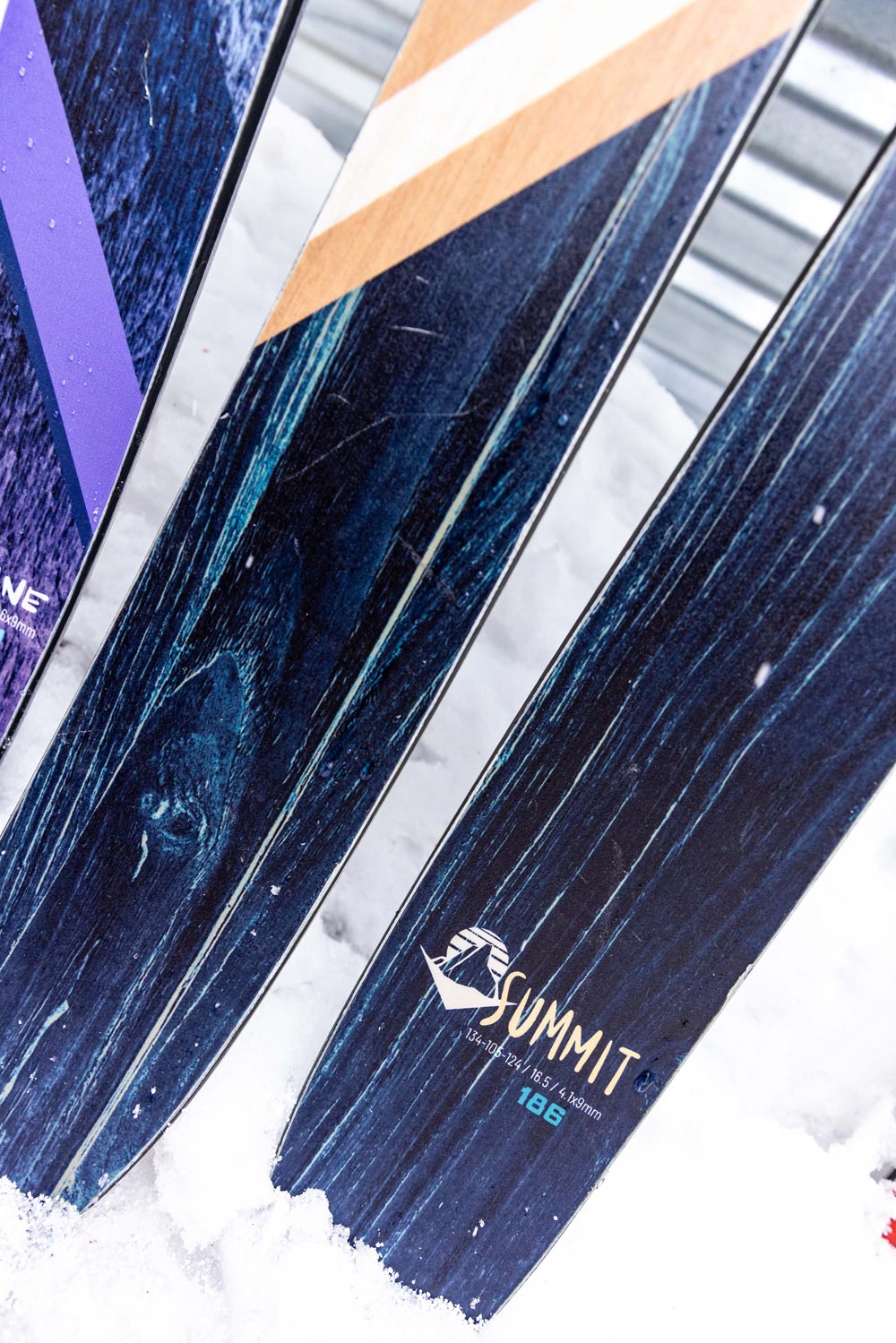 close-up image of the tails of the weston summit skis leaned up against a garage with snow of the ground