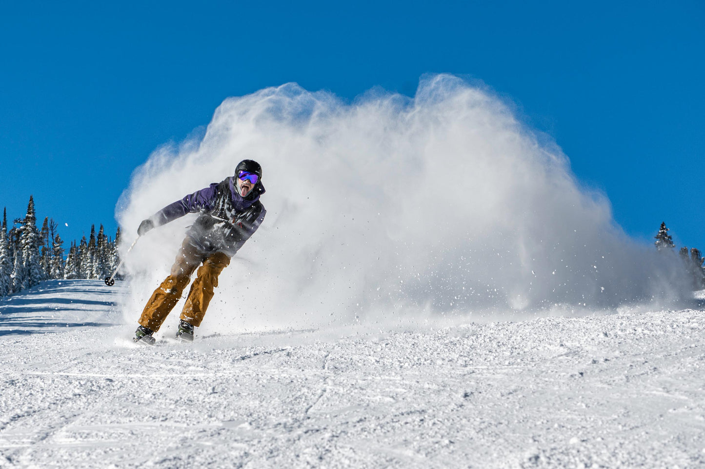 Skier on a ski resort sticking out his tongue and skiing on a pair of weston alpenglow skis with a big snow cloud behind him