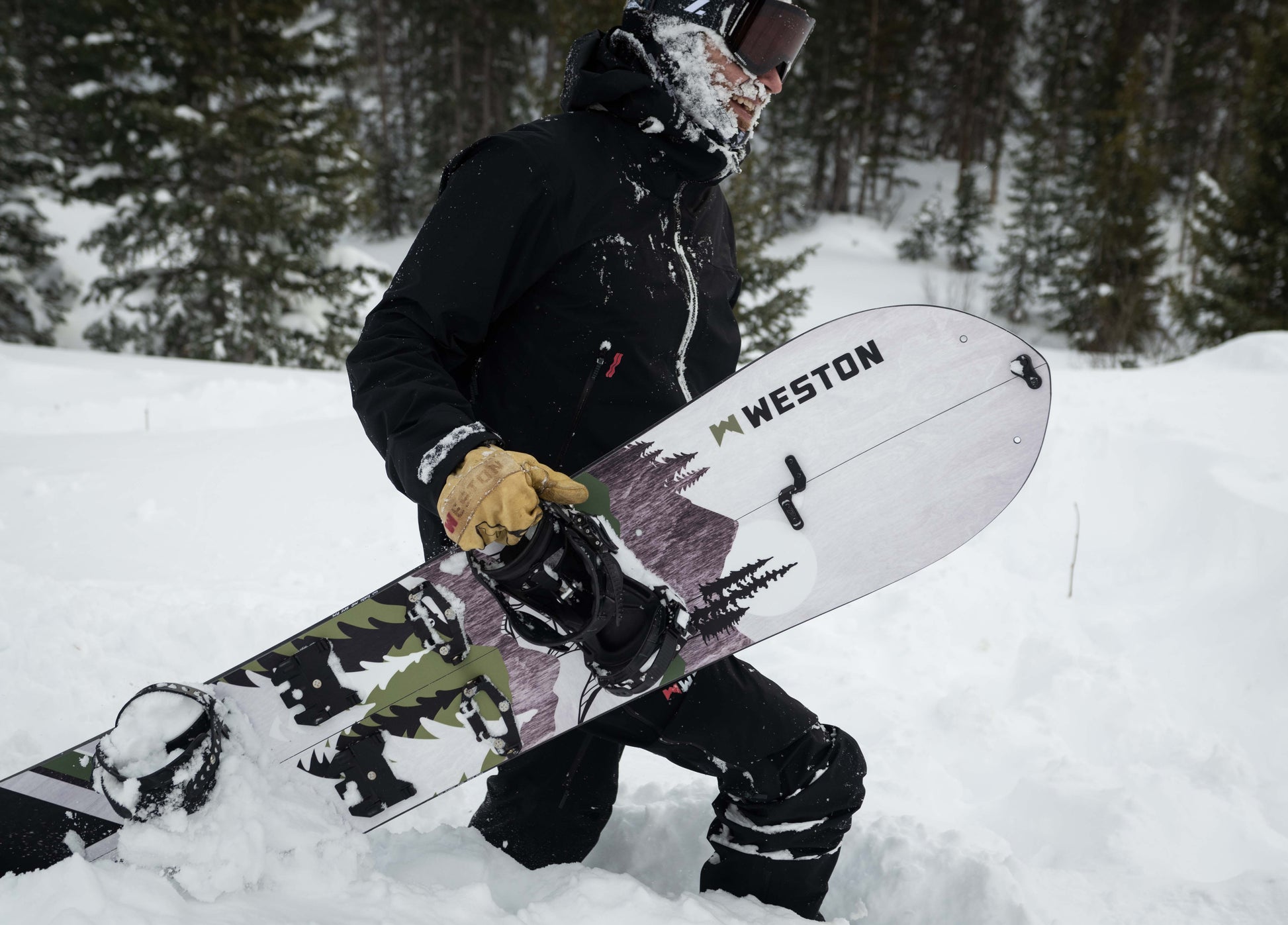 Splitboarder with a face full of snow holding a Weston backwoods carbon splitboard in a snowy forest setting