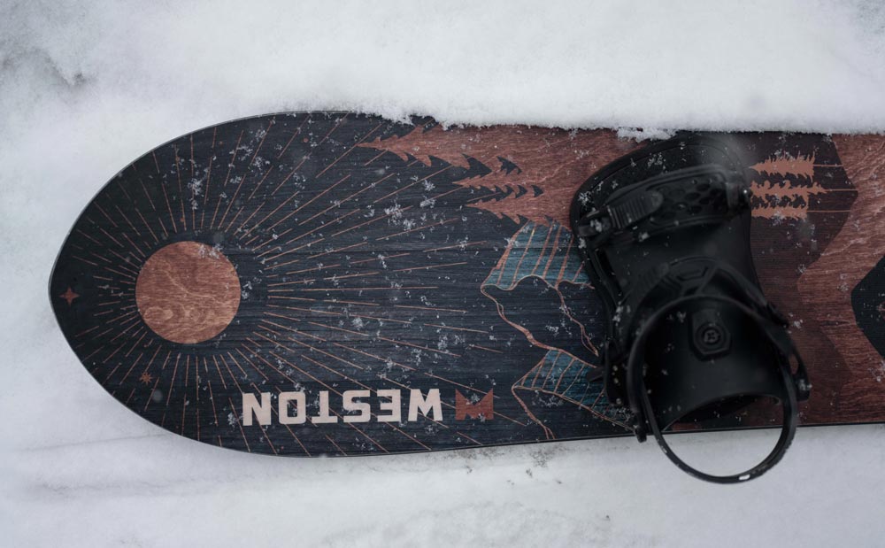 looking down a the weston eclipse snowboard on the snowy ground with a black union snowboard binding 