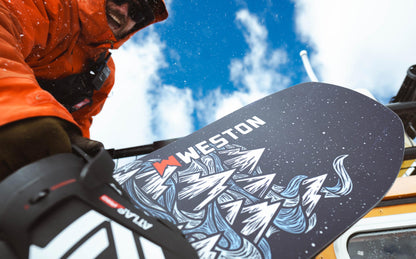Person holding the weston dream machine snowboard against the weston tucker snowcat background