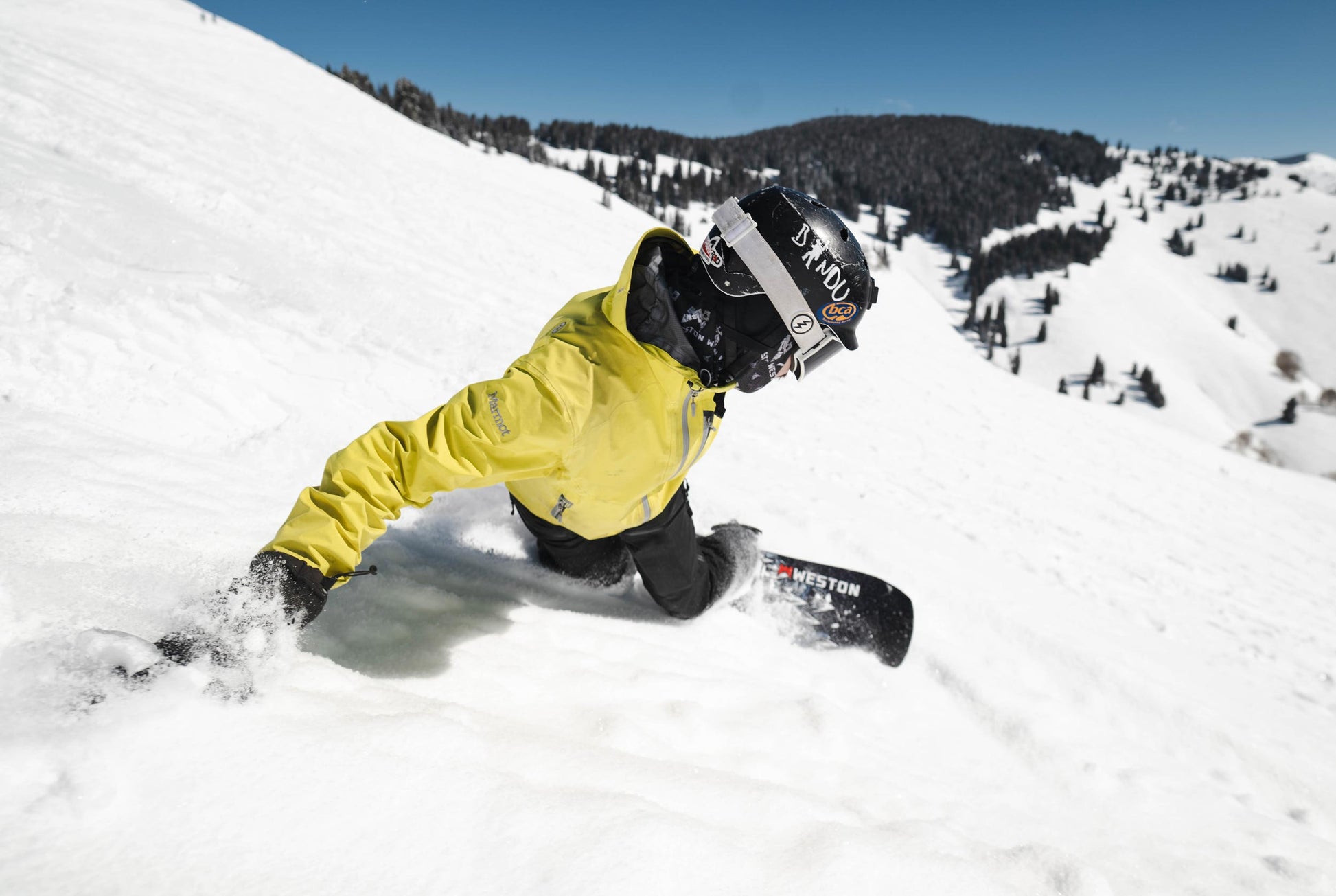 Person snowboarding down a hill on the weston dream machine snowboard with a helmet and goggles on a snowy landscape