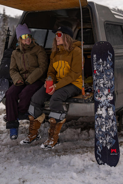 Two splitboarders sitting in the back of a van with the weston dream machine splitboard board leaning against it, in a snowy outdoor setting.