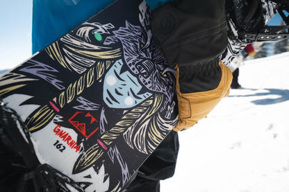 Snowboarder holding a weston gnarnia snowboard with a colorful viking woman design in a snowy environment