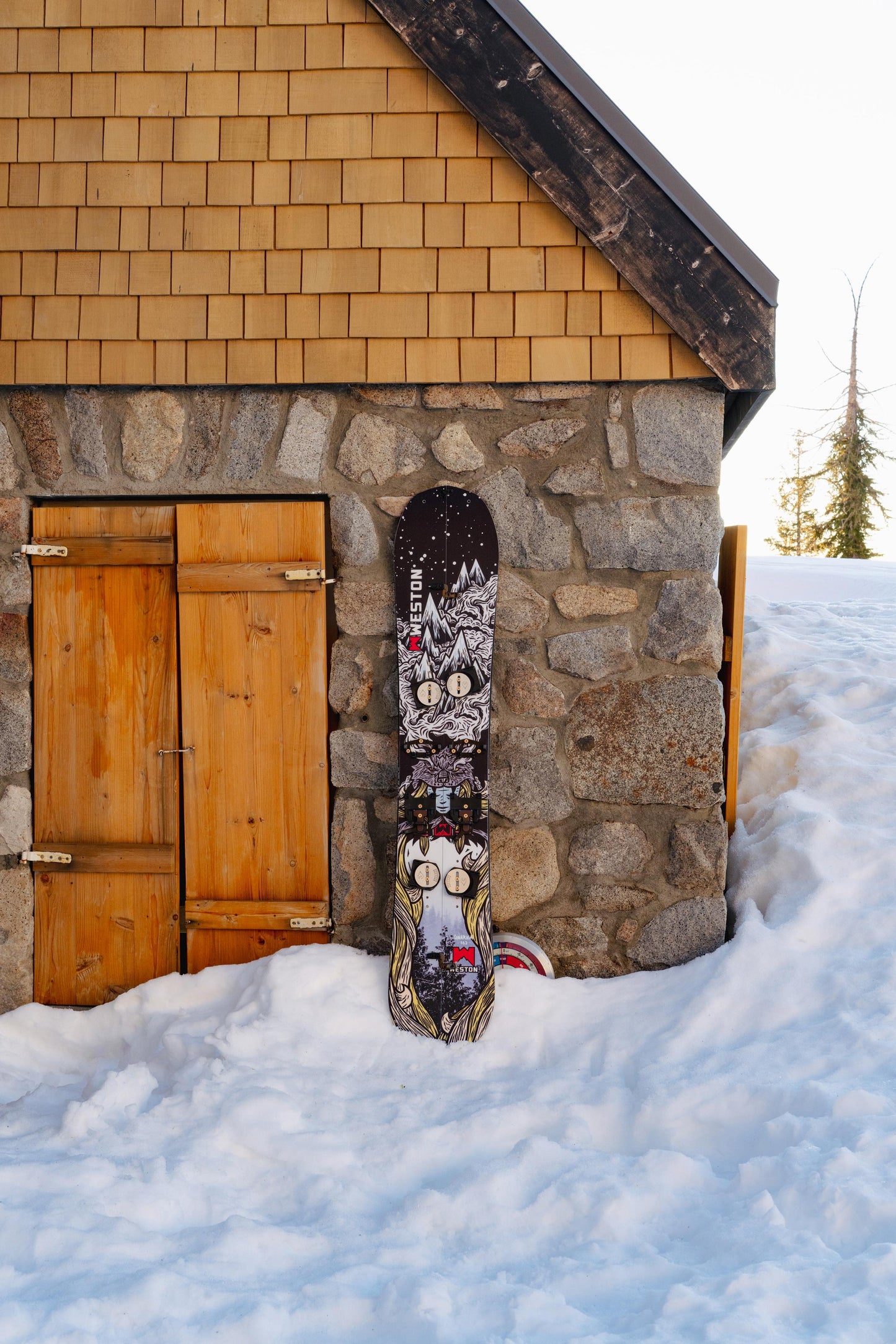 Weston Gnarnia Splitboard leaning against a stone and wooden cabin in the snow